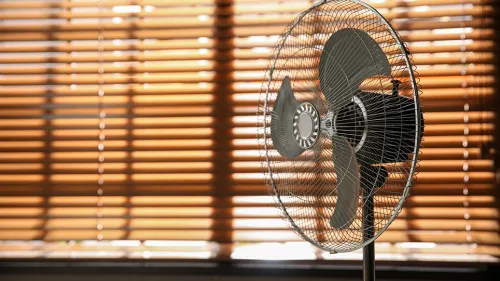 Fotografía de un ventilador cerca de persianas cerradas que bloquean la luz solar.