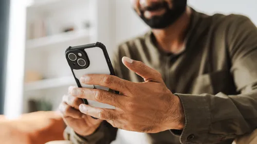 Photo of a young man sitting on a couch and using his cell phone.