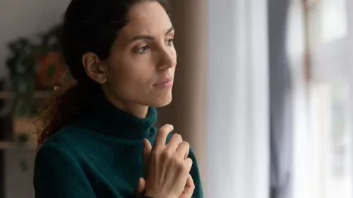 A woman is looking out a window with clasped hands