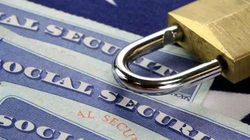 Three social security cards on a table with a padlock sitting just above them