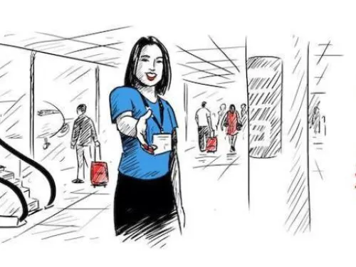 A woman wearing a blue blouse and a name tag is extending her hand for a handshake in an airport or transit terminal. People with luggage are seen in the background near escalators and departure gates, indicating a welcoming or assistance scene.