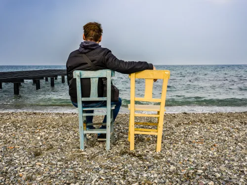 Photo of a man in a chair facing the sea beside an empty chair.
