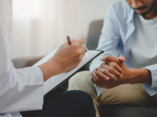 Photo of mental health professional taking notes from a male patient