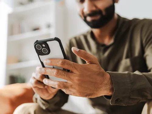 Photo of a young man sitting on a couch and using his cell phone.