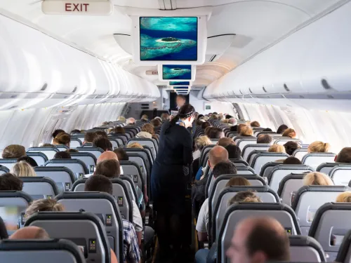 Interior of an airplane cabin with passengers seated in rows, a flight attendant in the aisle