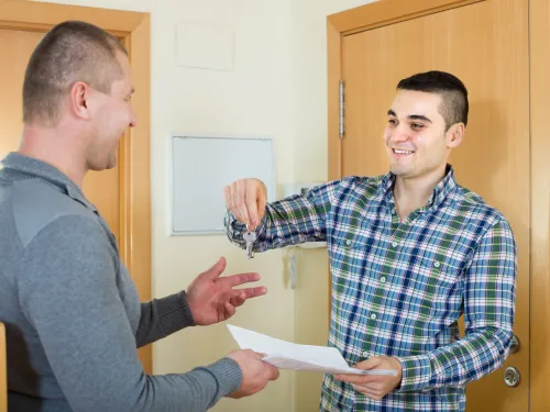 A smiling tenant receives the keys and lease agreement to his new apartment from a housing representative.