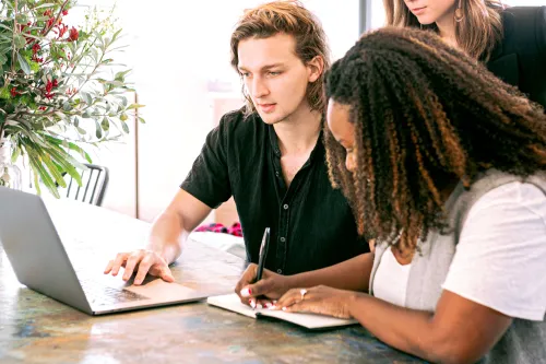 Man and two women working on a laptop and taking notes