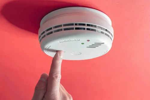 Fotografía del dedo de una persona presionando un botón en una alarma de humo para probarla.