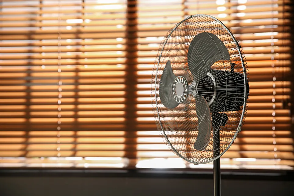 Fotografía de un ventilador cerca de persianas cerradas que bloquean la luz solar.