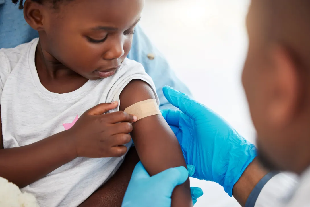 Photo of a doctor and a child with a band-aid on her arm after getting a vaccination.