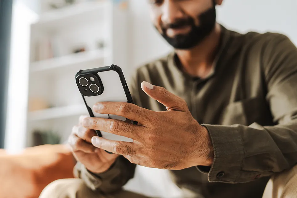 Photo of a young man sitting on a couch and using his cell phone.