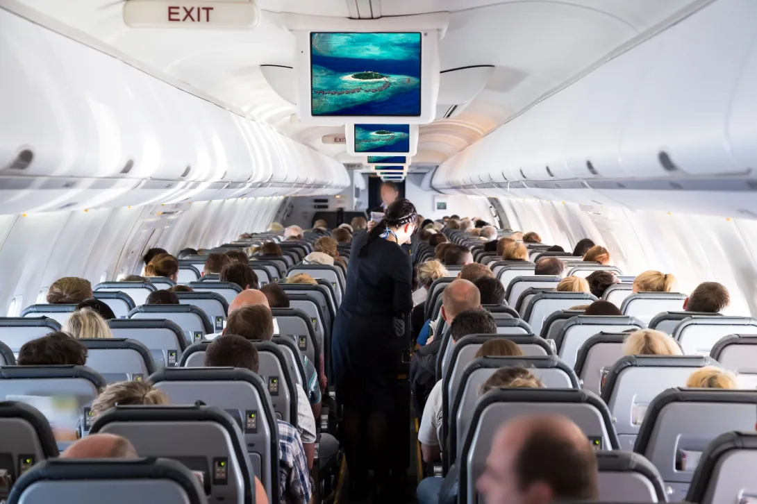Interior of an airplane cabin with passengers seated in rows, a flight attendant in the aisle