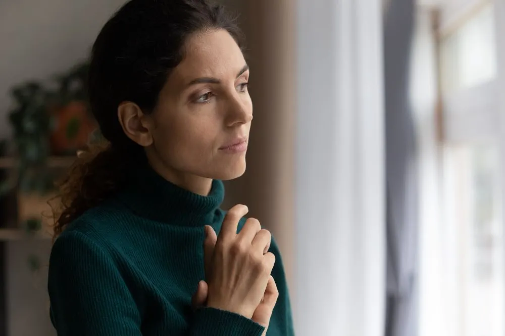 A woman is looking out a window with clasped hands