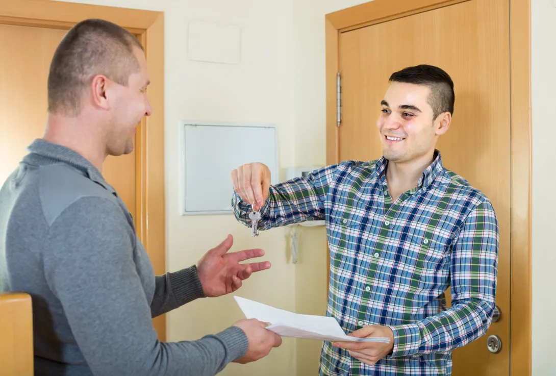 A smiling tenant receives the keys and lease agreement to his new apartment from a housing representative.