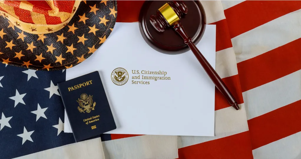 ​​A U.S. passport, a judge's gavel, and an envelope from U.S. Citizenship and Immigration Services are laid on an American flag.​ 